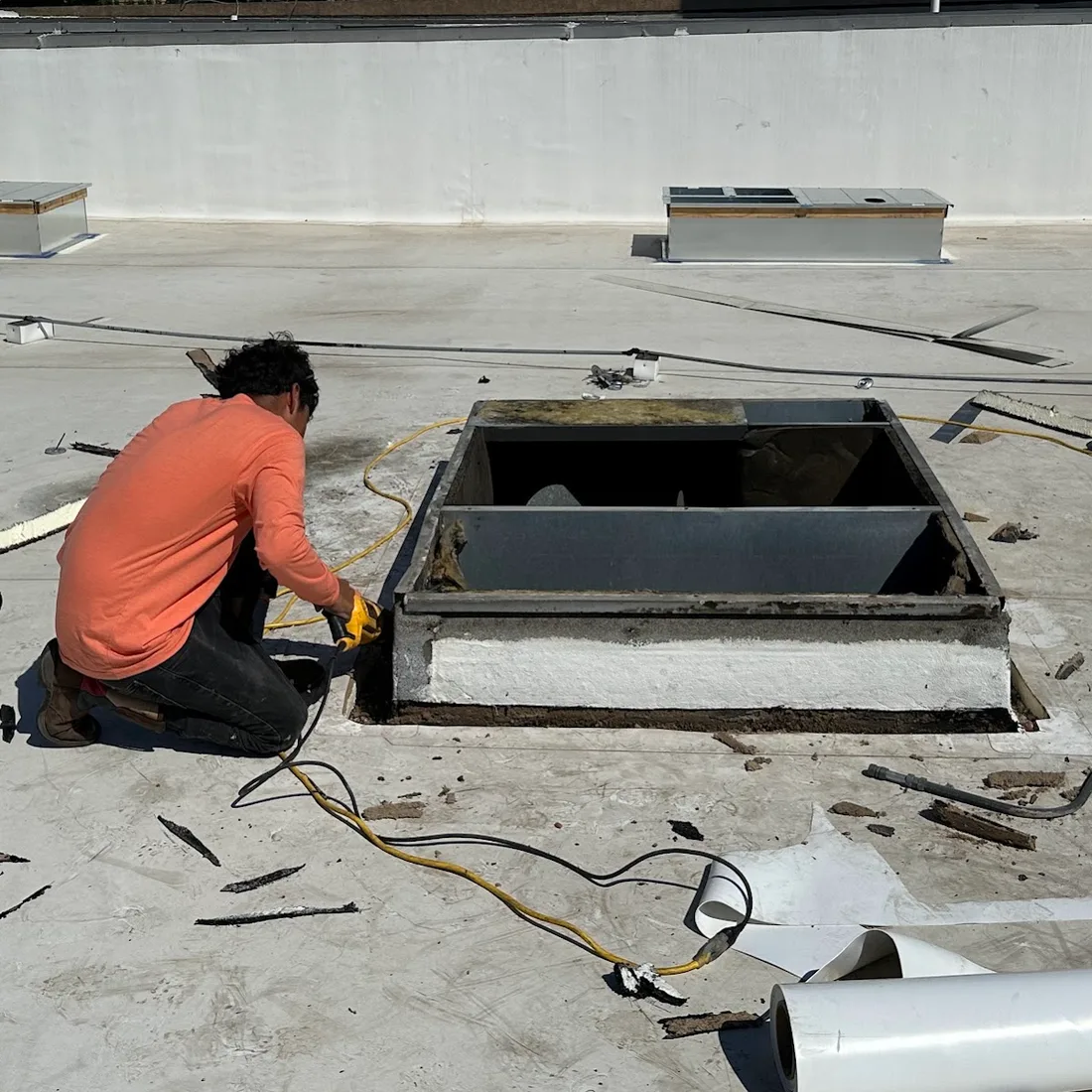 A roofer cutting the failed base flashing out of a rooftop equipment curb on a Houston commercial roof